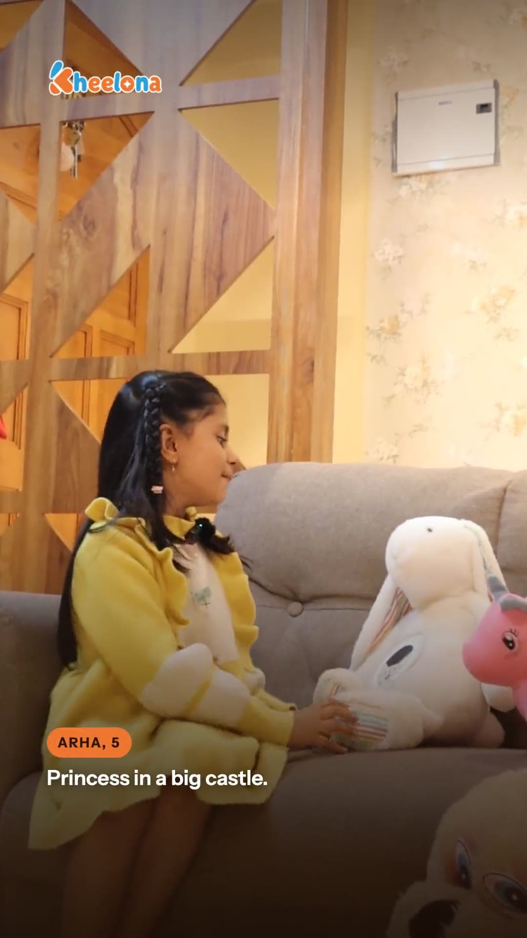 A girl on a sofa beside the cream Kheelu plush.