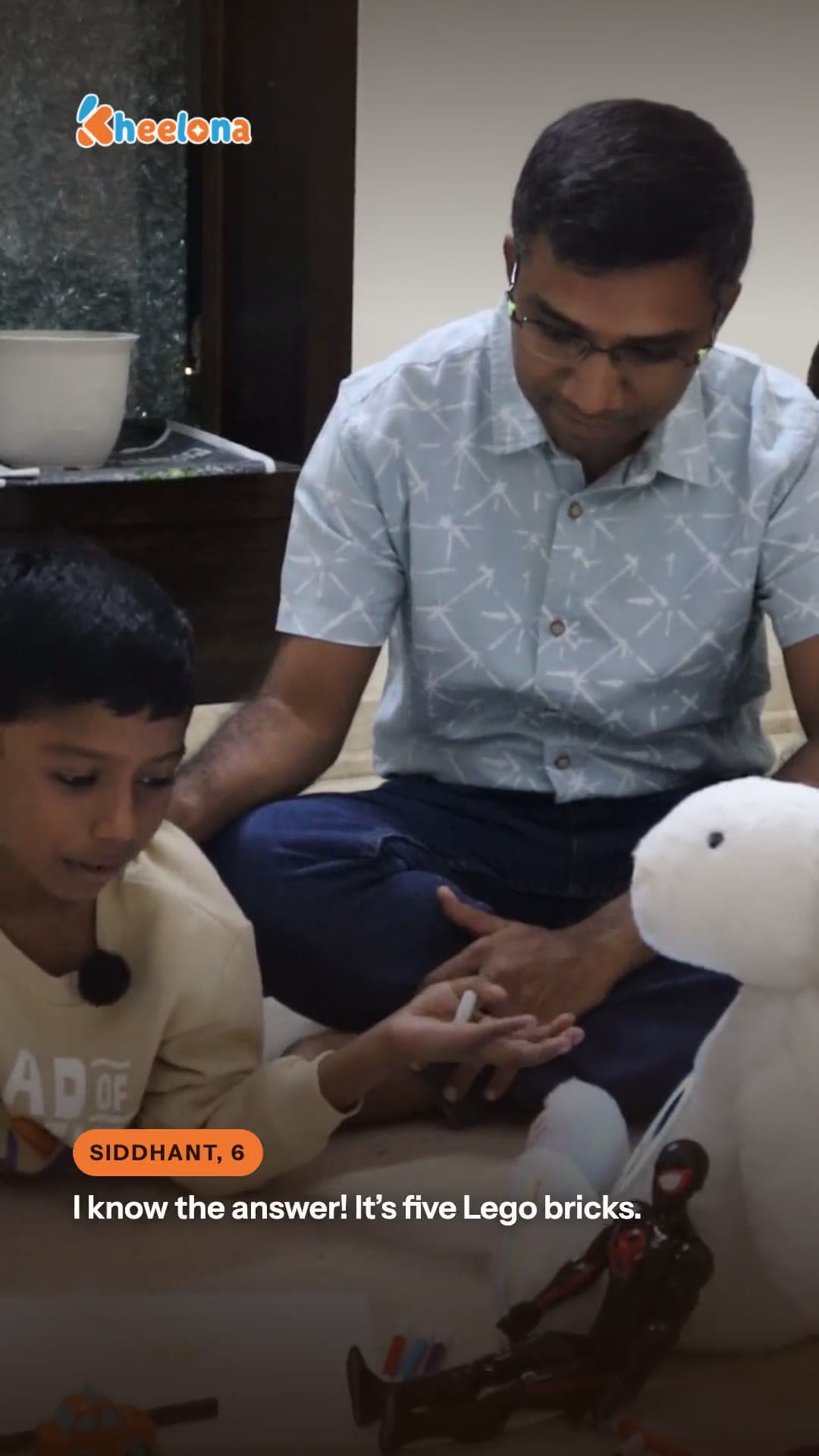 A boy on the floor with Lego bricks and the cream Kheelu plush.